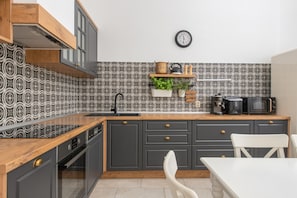 Una cocina moderna con encimera de madera, armarios grises, un lavamanos negro y un reloj en la pared.