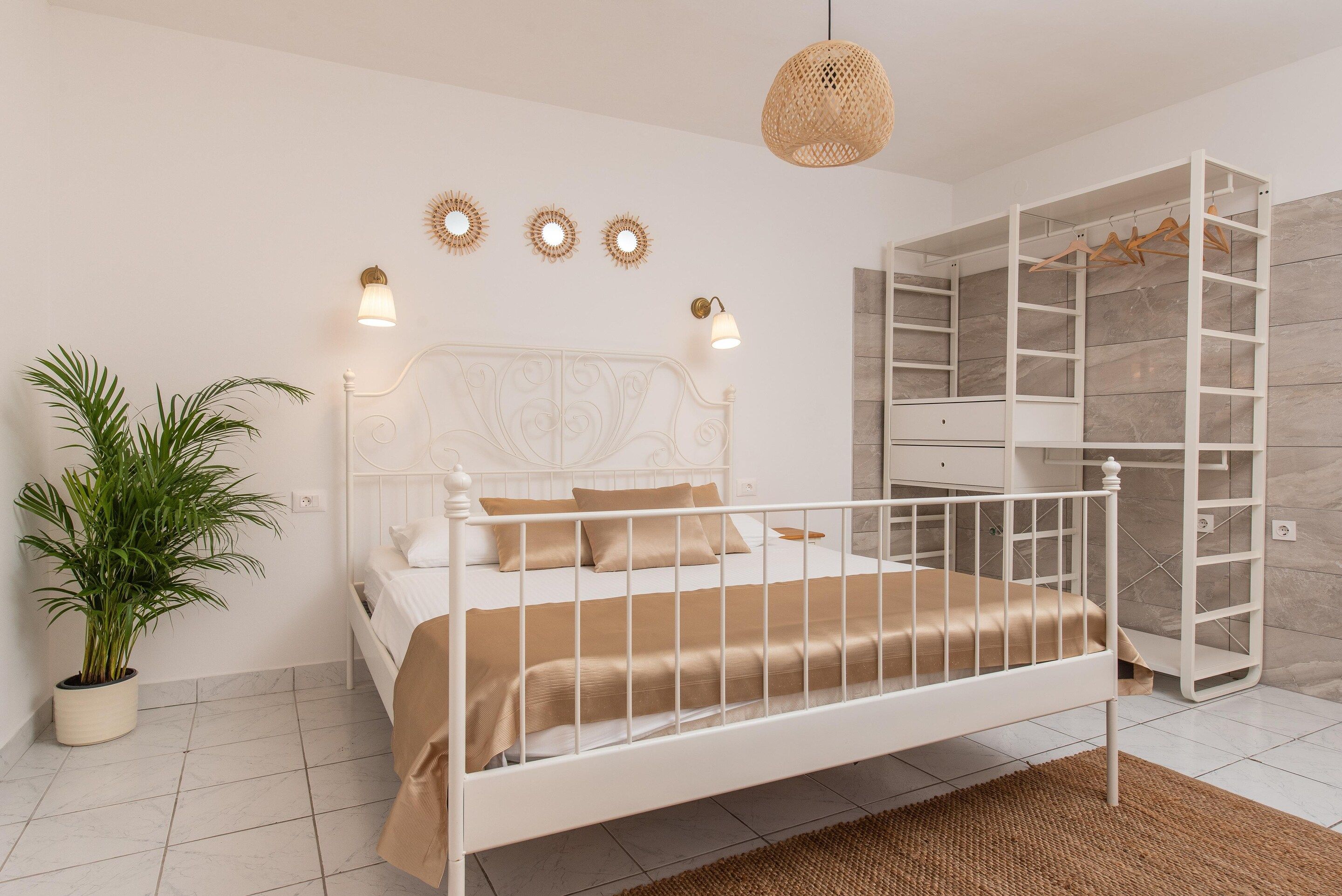 A bedroom with a white bed, a bedside plant, a hanging light fixture, and a built-in wardrobe with shelves.