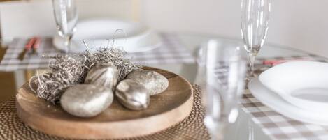 Una mesa de comedor dispuesta con platos blancos, cubiertos y un centro de mesa de madera con piedras y cuerda decorativa.