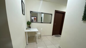A narrow hallway with a white desk, a chair, a potted plant, and a mirror on the wall. - Beautiful Bedroom in AlBarsha Near Metro (Dubai)