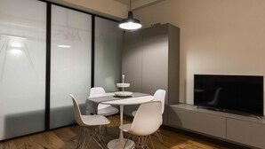 Una habitación moderna con una mesa redonda, sillas blancas, un televisor de pantalla plana y una lámpara colgante.
