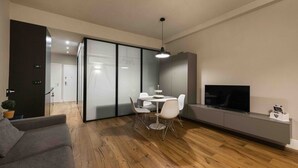 Una sala de estar moderna con un sofá, una mesa de comedor, sillas, un televisor y una puerta corredera que da a otra habitación.