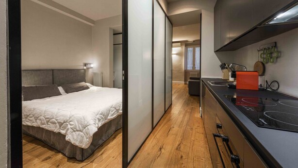Un dormitorio moderno con una cama y una puerta corrediza que da a una cocina con estufa.
