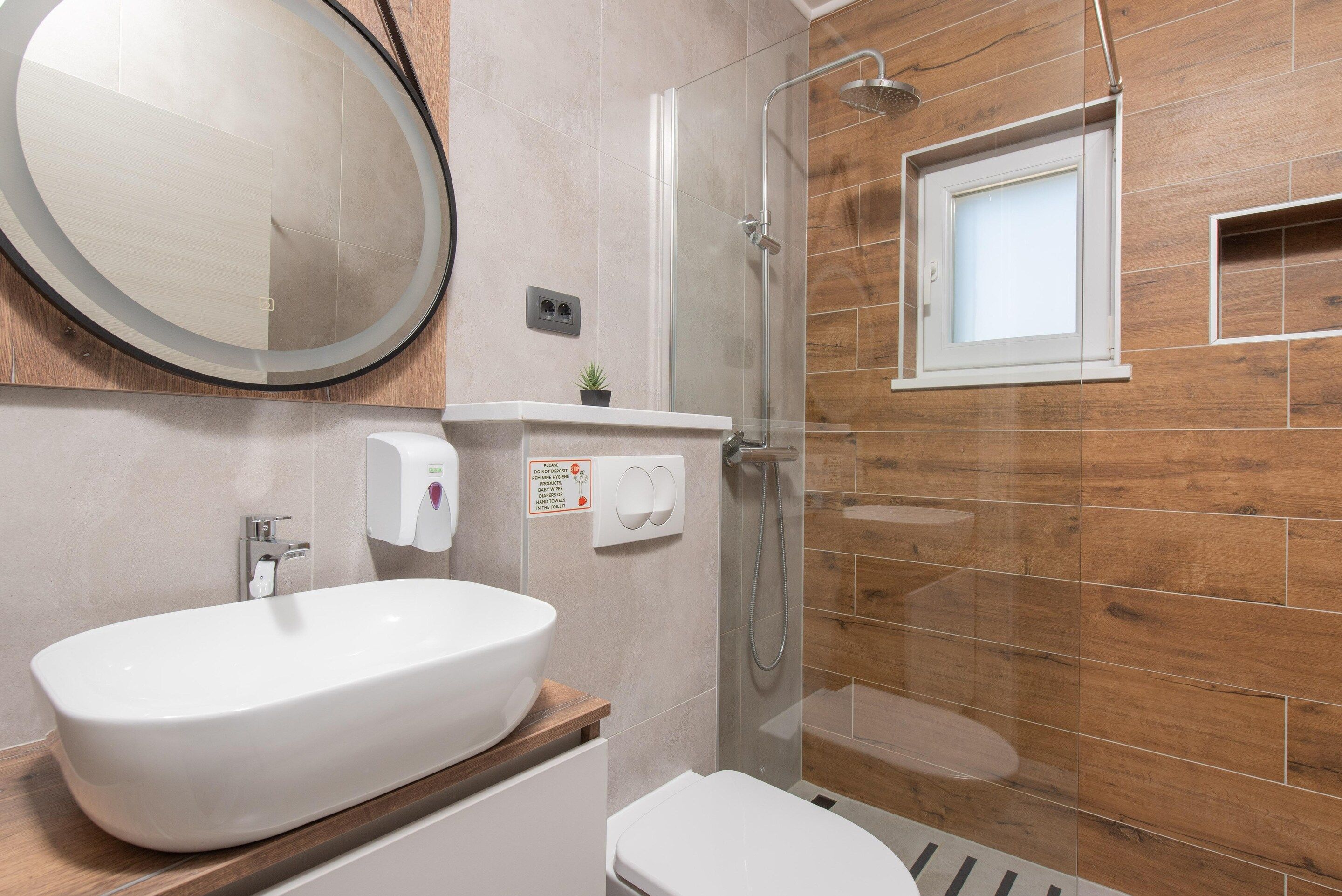 Une salle de bain moderne avec un grand lavabo ovale, des toilettes, une douche à parois de verre et un mur en bois.