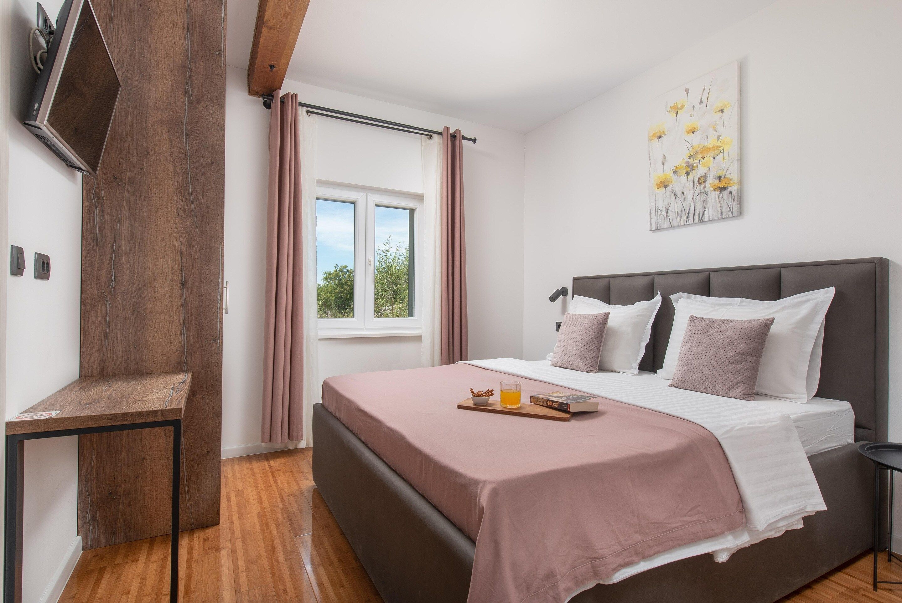 A bedroom with a bed, a bedside table, a window with curtains, and a painting on the wall.