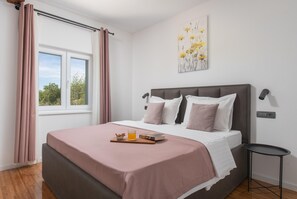 A bedroom with a bed, a bedside table, a window with curtains, and a wall-mounted artwork. - Stylish Villa in Lovrec With Sauna for 10 (Lovreć)