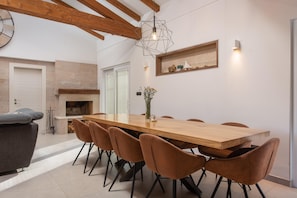 A dining area with a wooden table and chairs, a fireplace, and a wall-mounted shelf with decorative items. - Stylish Villa in Lovrec With Sauna for 10 (Lovreć)