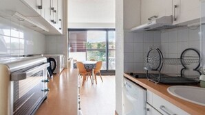 A modern kitchen with white cabinets, a stainless steel range, and a dining area with a table and chairs. - 33m2 apartment in the heart of the dunes, 5 minutes from the beach (Le Touquet)