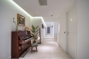A hallway with a piano, a small stool, and a potted plant. - Vivi Milano - Modern 5BR Apartment with Free Parking & Terrace Near the Fair (Baranzate)