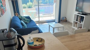 Ett kompakt kök med en bänkskiva i trä, en kaffebryggare och en skål med en sked. Det finns en skjutdörr i glas som leder ut till en balkong med ett bord och stolar.