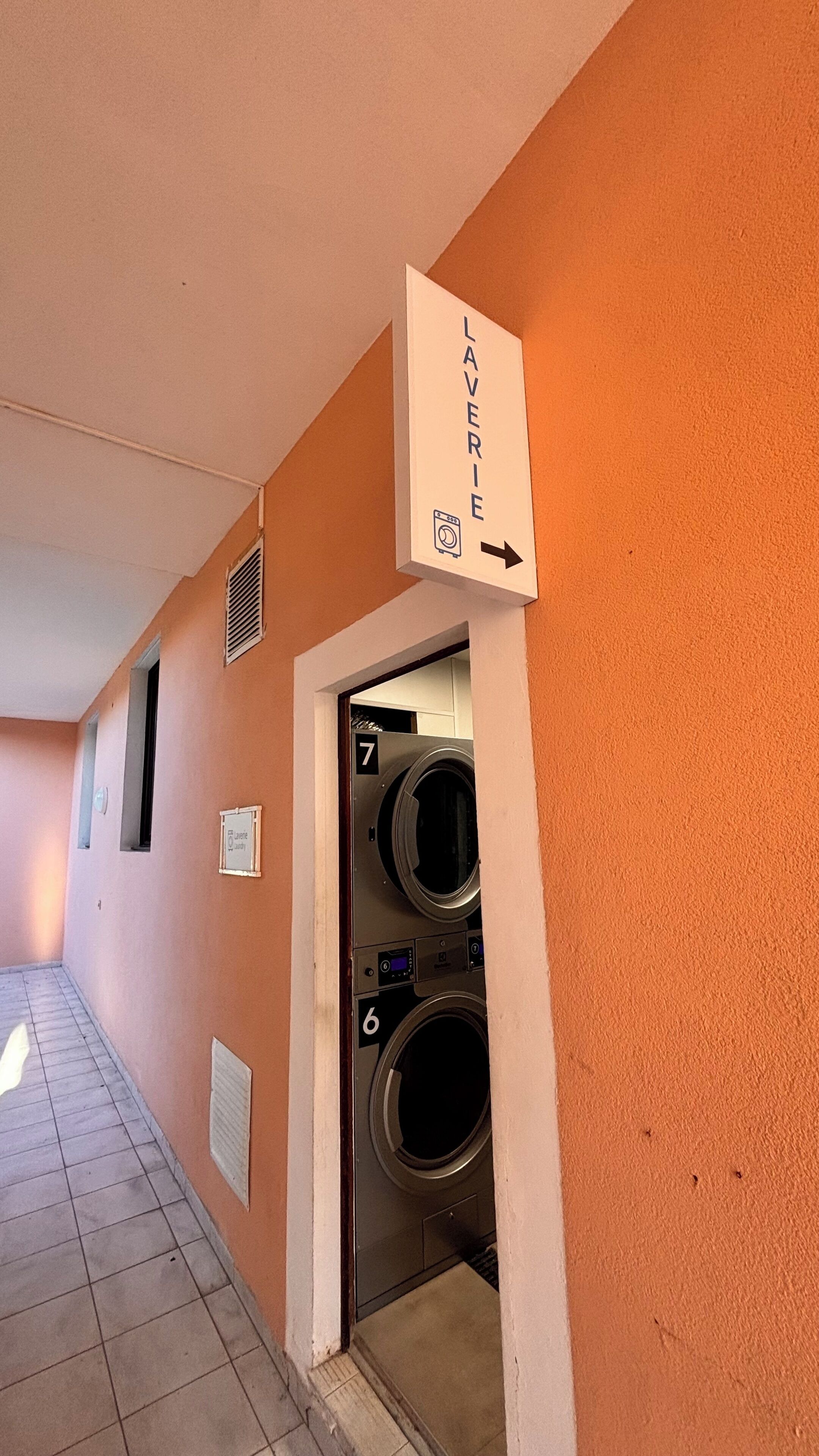 Une buanderie équipée de deux machines à laver, numérotées 6 et 7, et d’un panneau indiquant la direction à suivre pour s’y rendre.