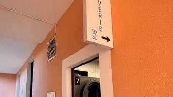 Une buanderie équipée de deux machines à laver, numérotées 6 et 7, et d’un panneau indiquant la direction à suivre pour s’y rendre.
