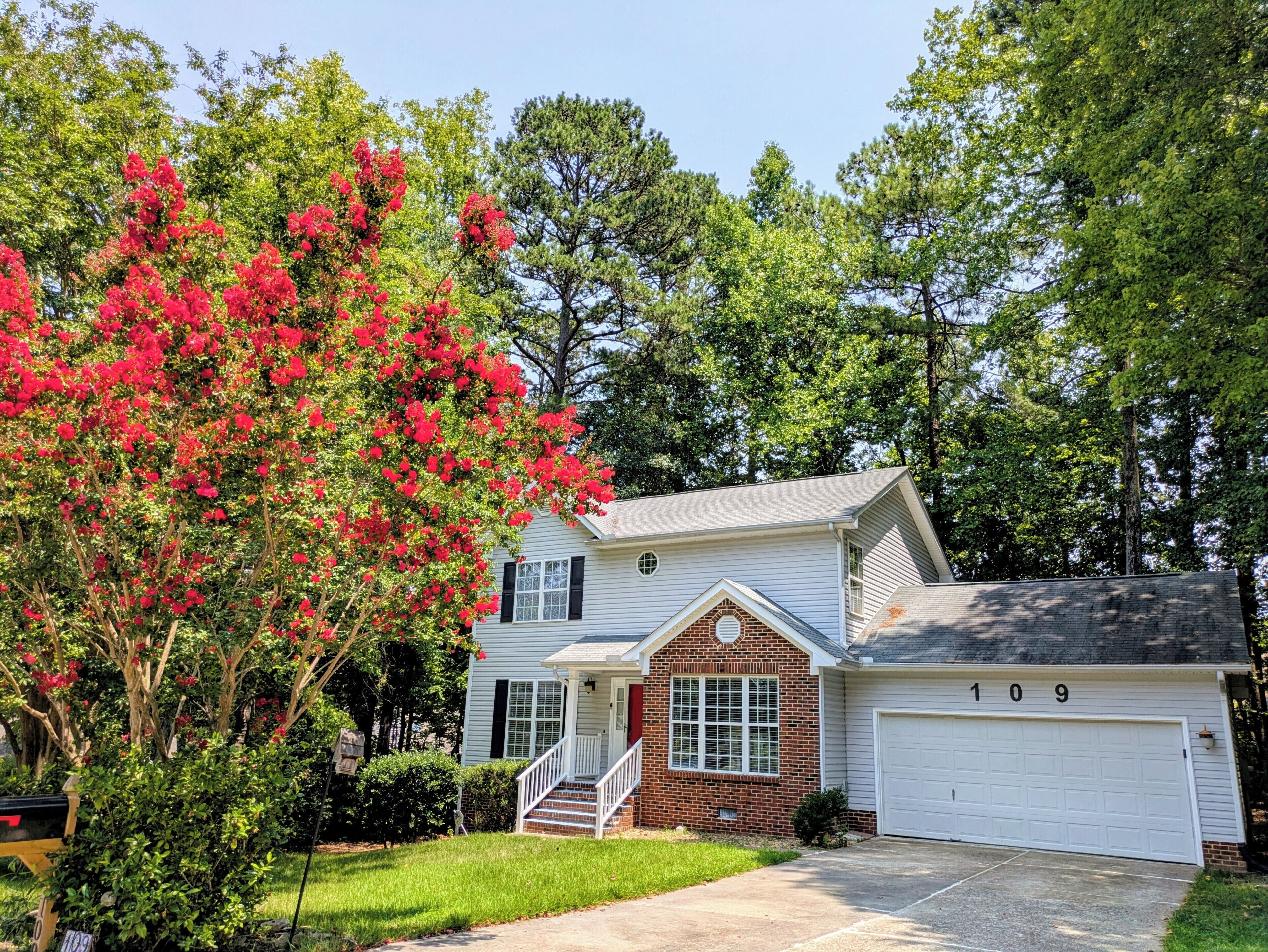 A two-story house with a garage, a front porch, and a red flowering tree.