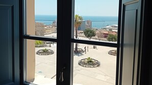 Une vue à travers une fenêtre donnant sur un paysage urbain, avec des bâtiments et une étendue d’eau.