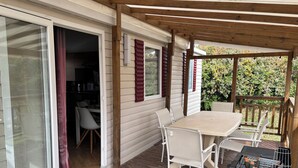 A covered patio with a table and chairs, a grill, and a sliding glass door leading to an interior space. - Mobile Home 291, 4-Star Siblu Campground, Wi-Fi, Air Conditioning  (Lattes)