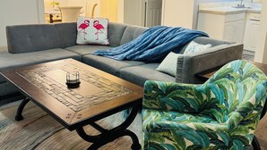 A living room with a grey sofa, a wooden coffee table, and a green patterned armchair. - Economical & Gorgeous 2-bedroom townhome – Peaceful, Safe & Near the Lake (Garland)