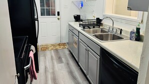 A compact kitchen with a sink, dishwasher, and a window with blinds. - Economical & Gorgeous 2-bedroom townhome – Peaceful, Safe & Near the Lake (Garland)