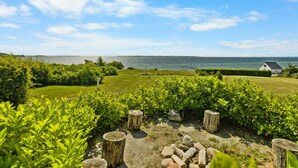 Et kystlandskab med græsareal, træstammer og en hvid bygning ved havet.