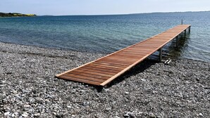 En træbro, der strækker sig ud i roligt vand, omgivet af en stenet strand.