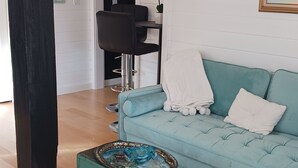 Un salon avec un canapé de couleur turquoise, un tapis à rayures colorées, une table en verre décorative et un lustre.