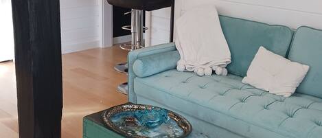 Una sala de estar con un sofá color turquesa, un tapete a rayas de colores, una mesa de vidrio decorativa y una araña.