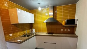 Een kleine keuken met witte kastjes, een magnetron en een roestvrijstalen afzuigkap.