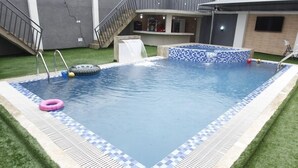 Een rechthoekig zwembad met betegelde rand, een kleine jacuzzi en een trap naar een hoger gelegen terras.