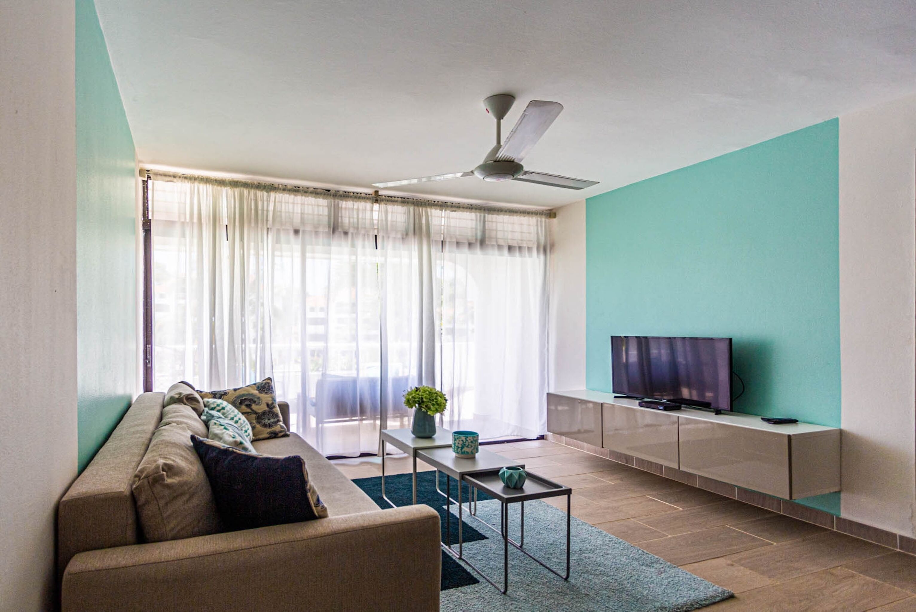 A living room with a sofa, a coffee table, a TV on a stand, and a ceiling fan.