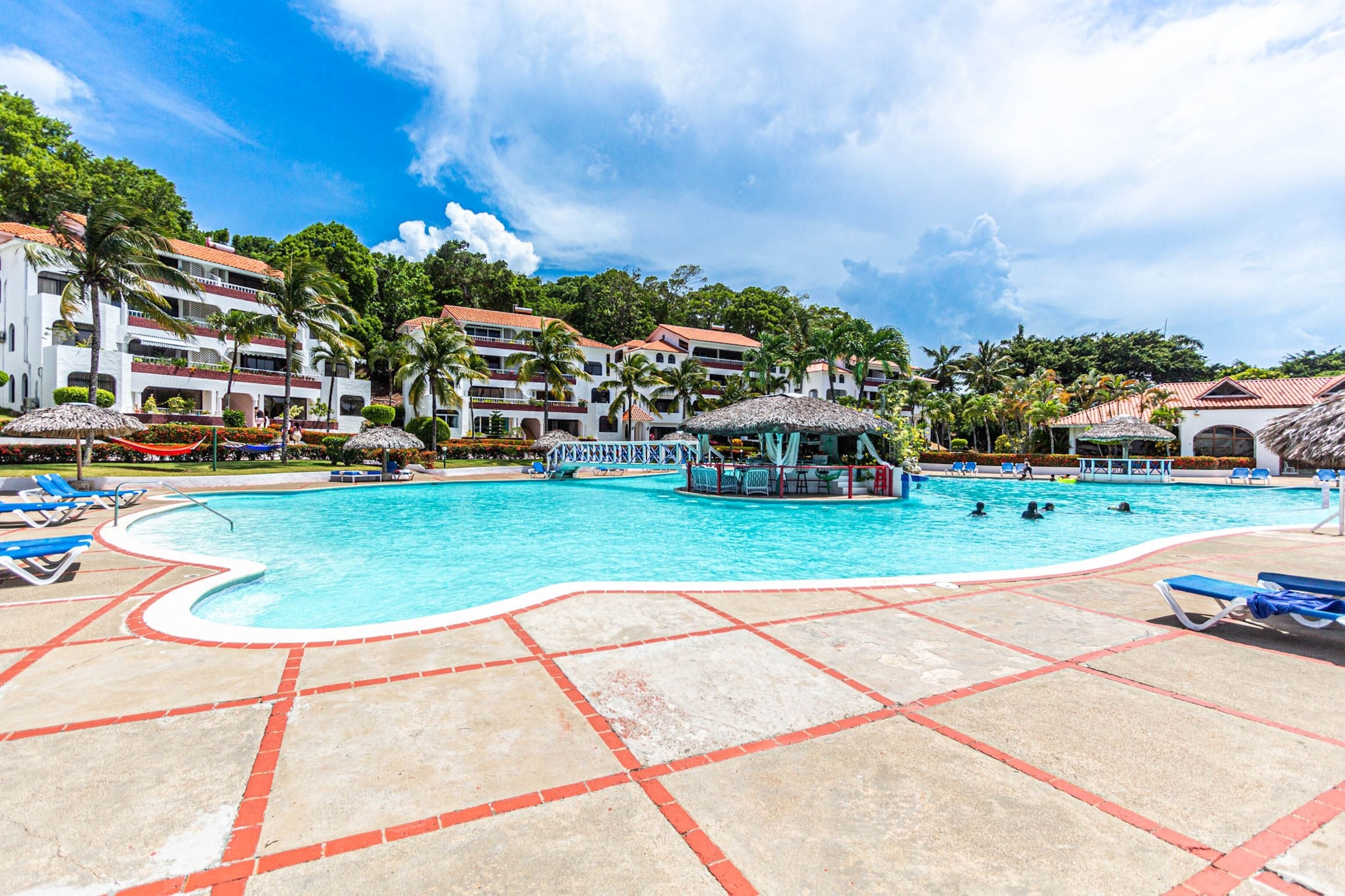 A swimming pool with lounge chairs, a gazebo, and a hotel building in the background.