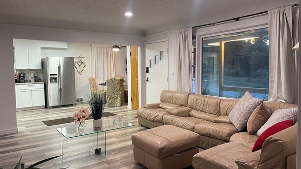 Una sala de estar moderna con un sofá, una mesa de centro de vidrio y una cocina al fondo.