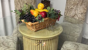 Una habitación con una mesa redonda de madera, una cesta de mimbre con frutas y verduras, y una planta en maceta.