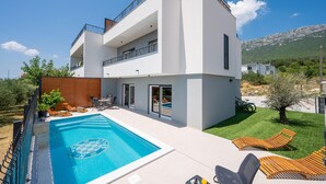 Una moderna casa a due piani con piscina, area salotto esterna e vista sul paesaggio circostante.