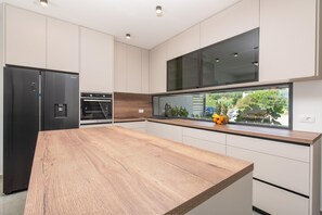 Eine moderne Küche mit einer Holz Arbeitsplatte, Edelstahlgeräten und einem großen Fenster mit Blick auf Grünflächen.