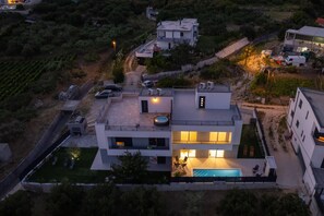 Ein modernes, mehrstöckiges Wohngebäude mit Pool auf dem Dach, einem gepflegten Rasen und einem Weinberg im Hintergrund.