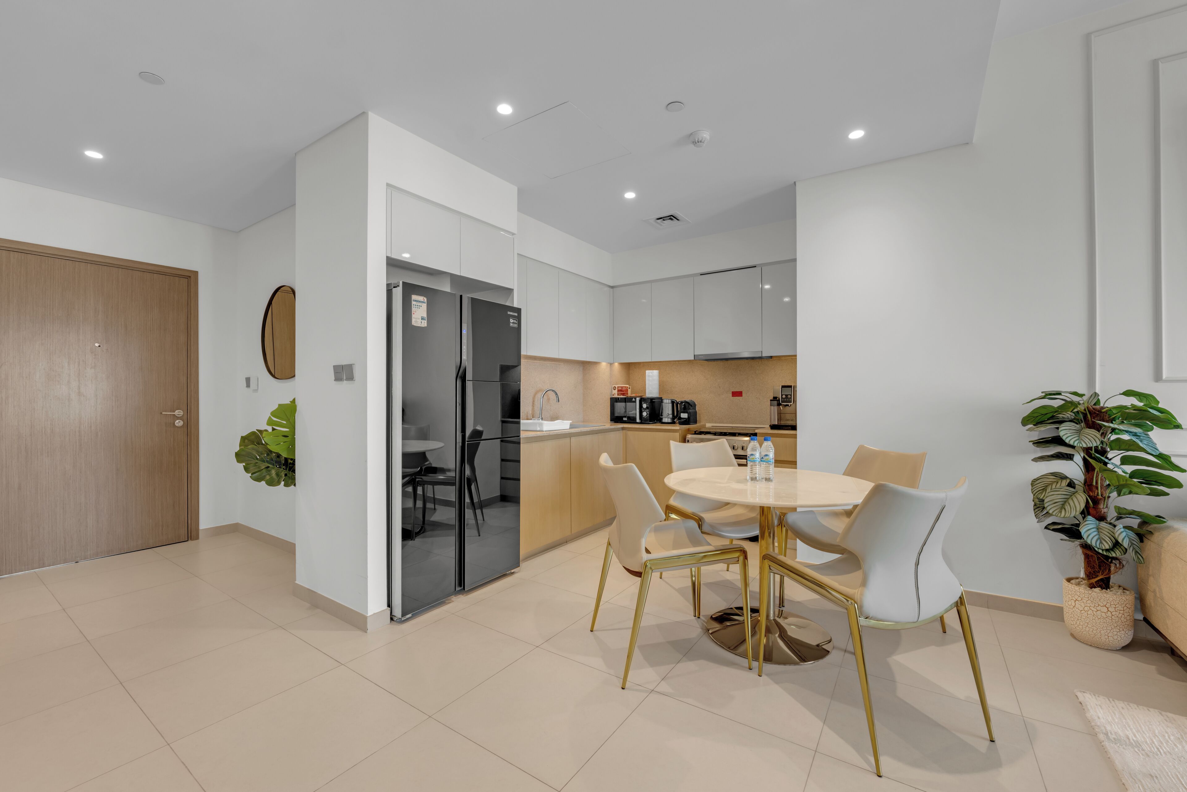 A modern kitchen with white cabinets, a dining area with a round table and chairs, and a wooden door.