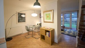 Et værelse med et spisebord, stole, en reol, en gulvlampe og et indrammet billede på væggen.