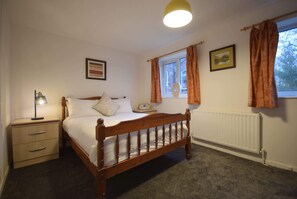 Ein Schlafzimmer mit einem hölzernen Bett, einem Nachttisch mit Lampe, einem Fenster mit Vorhängen und einem Heizkörper.