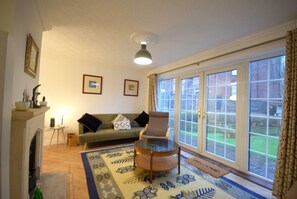 A living room with a sofa, armchair, and a glass-top coffee table. There is a fireplace, a rug, and a window with a view of the garden. - Cosy 2BDR House with Driveway Near Manchester (Manchester)