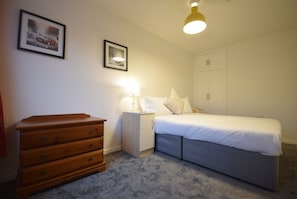 A bedroom with a bed, dresser, nightstand, lamp, and two framed pictures on the wall. - Cosy 2BDR House with Driveway Near Manchester (Manchester)