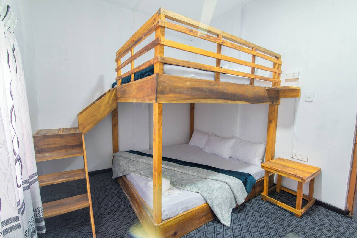 Une chambre avec un lit superposé, une petite échelle en bois, une petite table en bois et un sol à motifs.