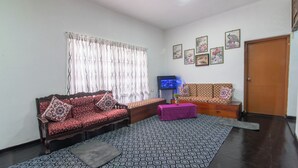 Uma sala de estar com sofá, um banquinho, televisão e tapete estampado.