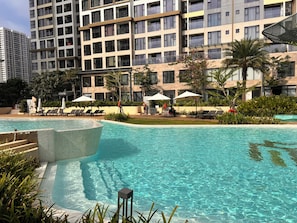 A swimming pool with lounge chairs and umbrellas, surrounded by greenery and modern buildings.