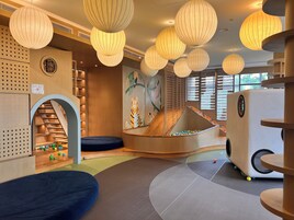 Uma área de recreação infantil com escorrega, rede de escalada e bolas coloridas.