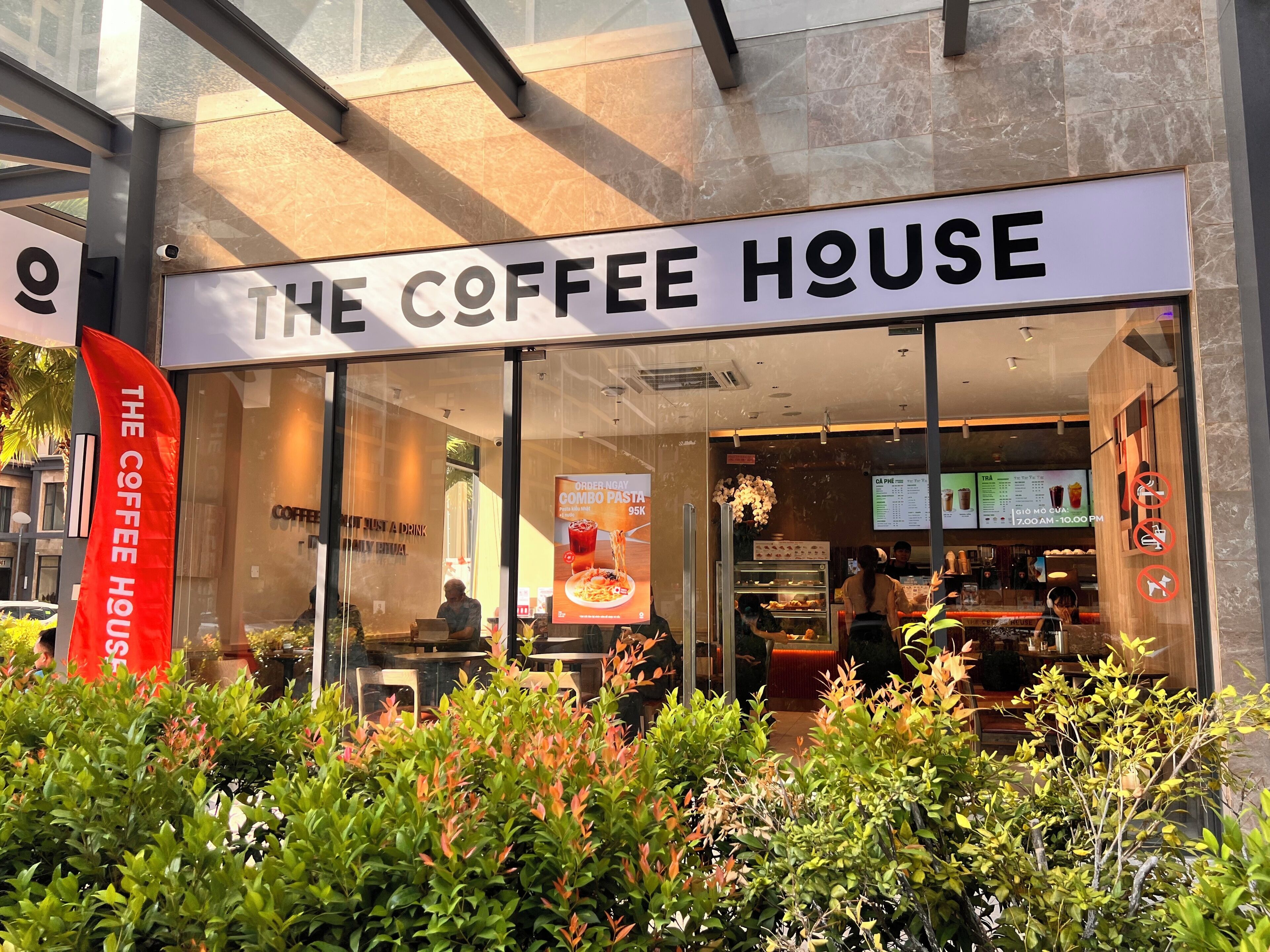 A coffee shop named 'The Coffee House' with a glass storefront, a menu board inside, and a red banner outside.