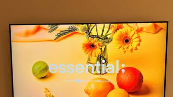 Ein Fernsehbildschirm zeigt ein lebhaftes Bild von Zitrusfrüchten und Blumen, mit dem Wort 'essential' deutlich sichtbar.