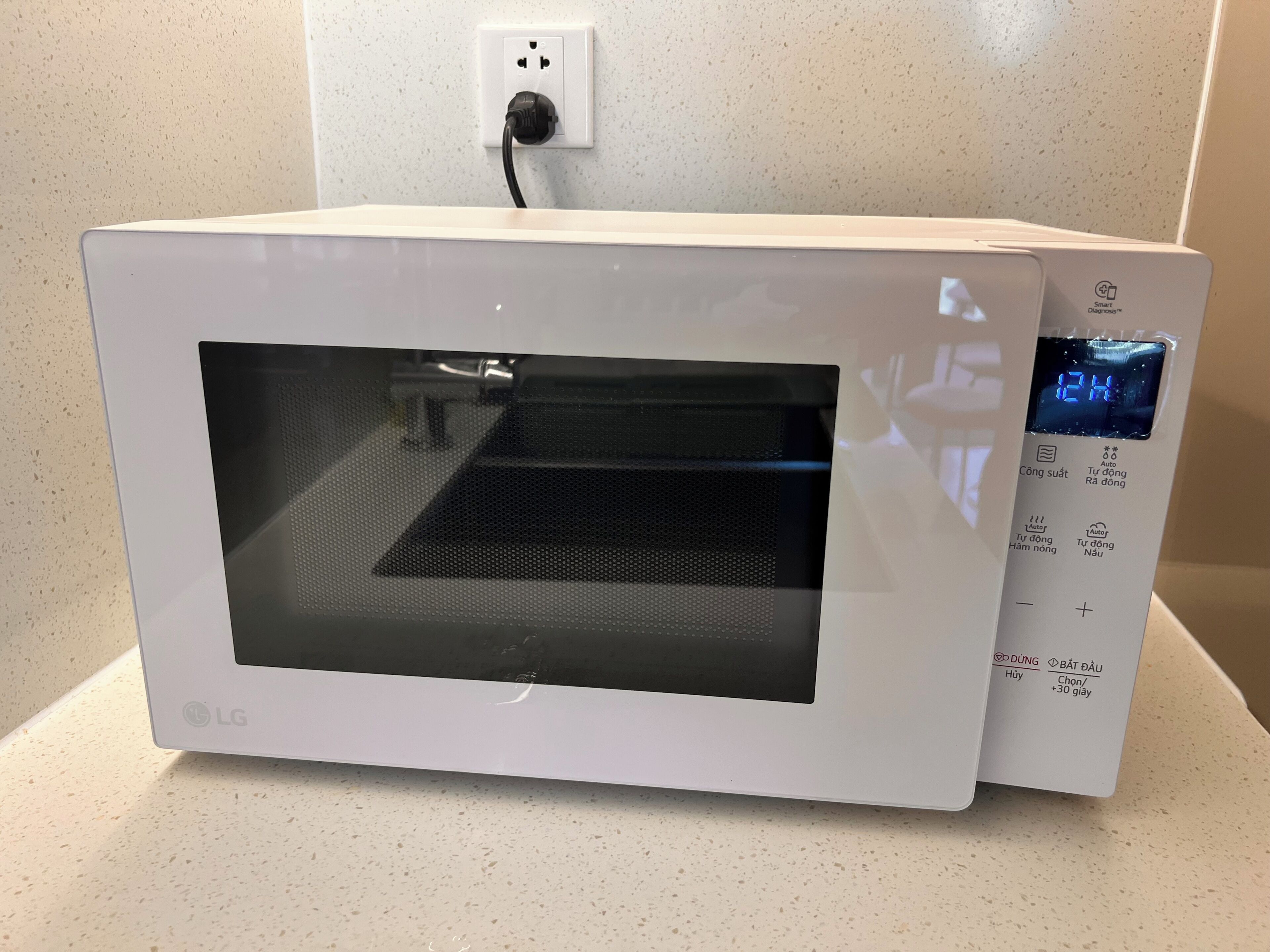 A white microwave oven with a digital display and control panel, connected to a power outlet.
