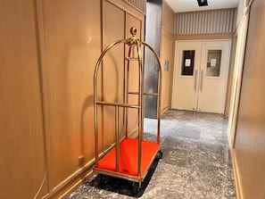 Un couloir avec un chariot doré, une porte dotée d’un clavier numérique et un sol carrelé.