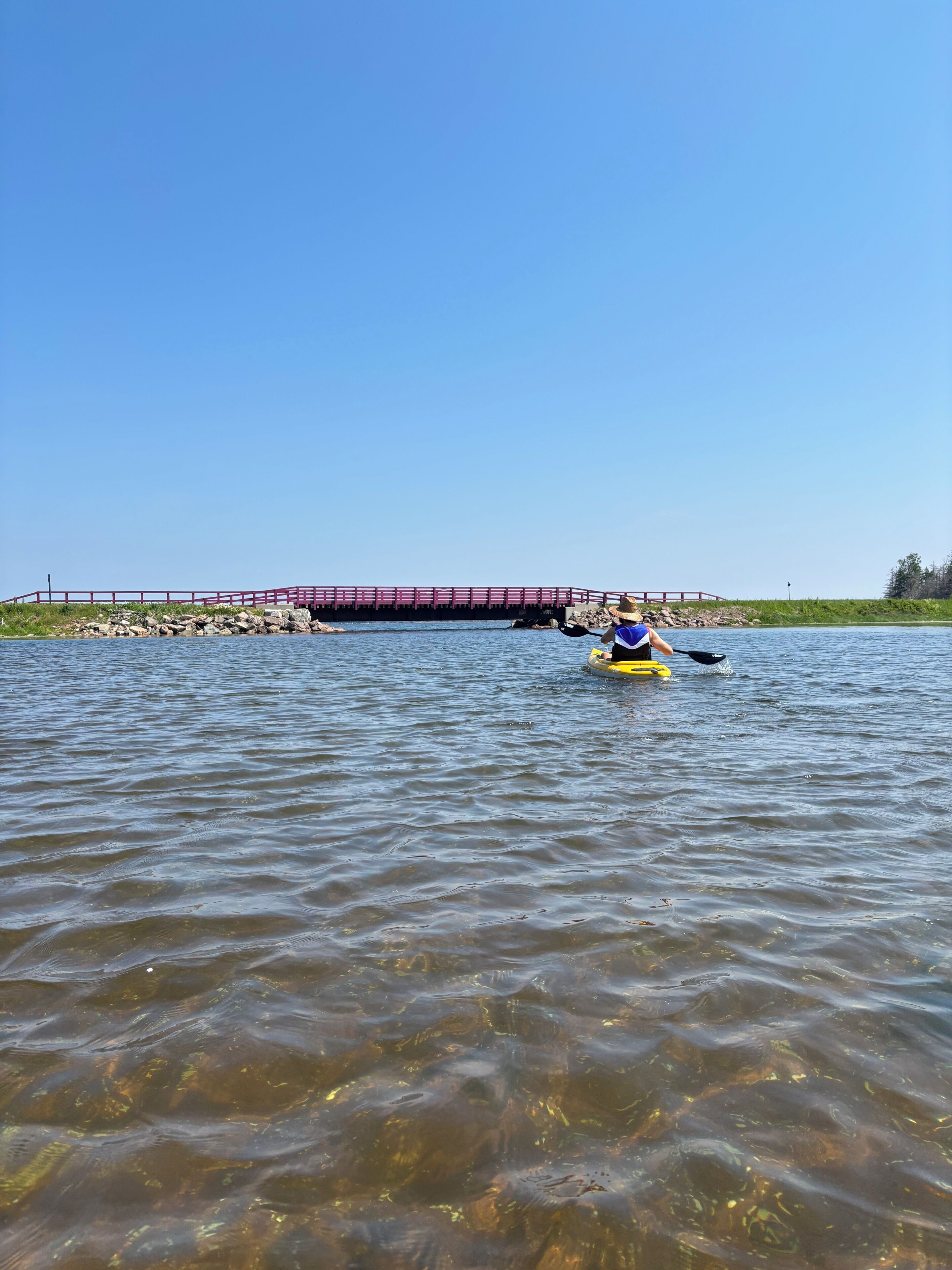 A calm body of water with a person paddling on a yellow raft.