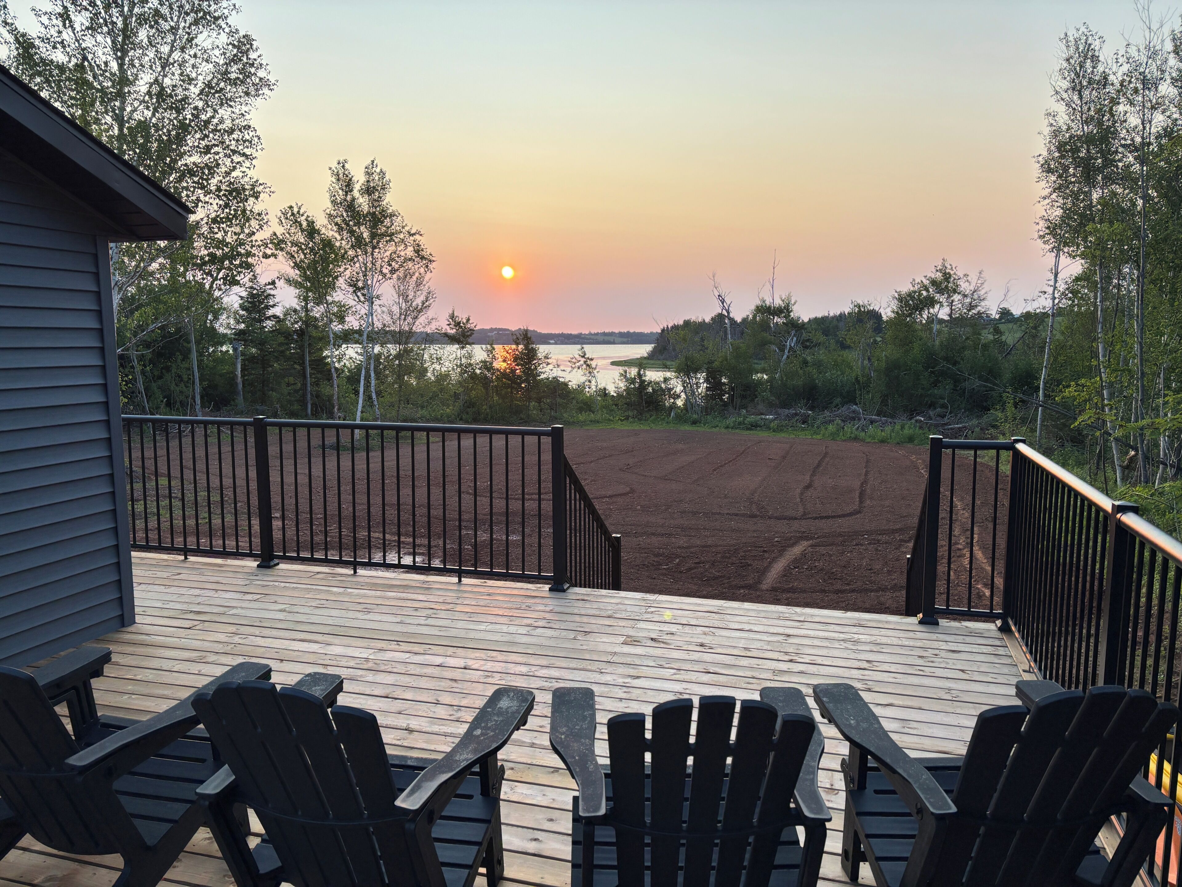 A deck with chairs and a view of the sunset over a body of water.