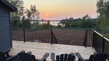A deck with chairs and a view of the sunset over a body of water.